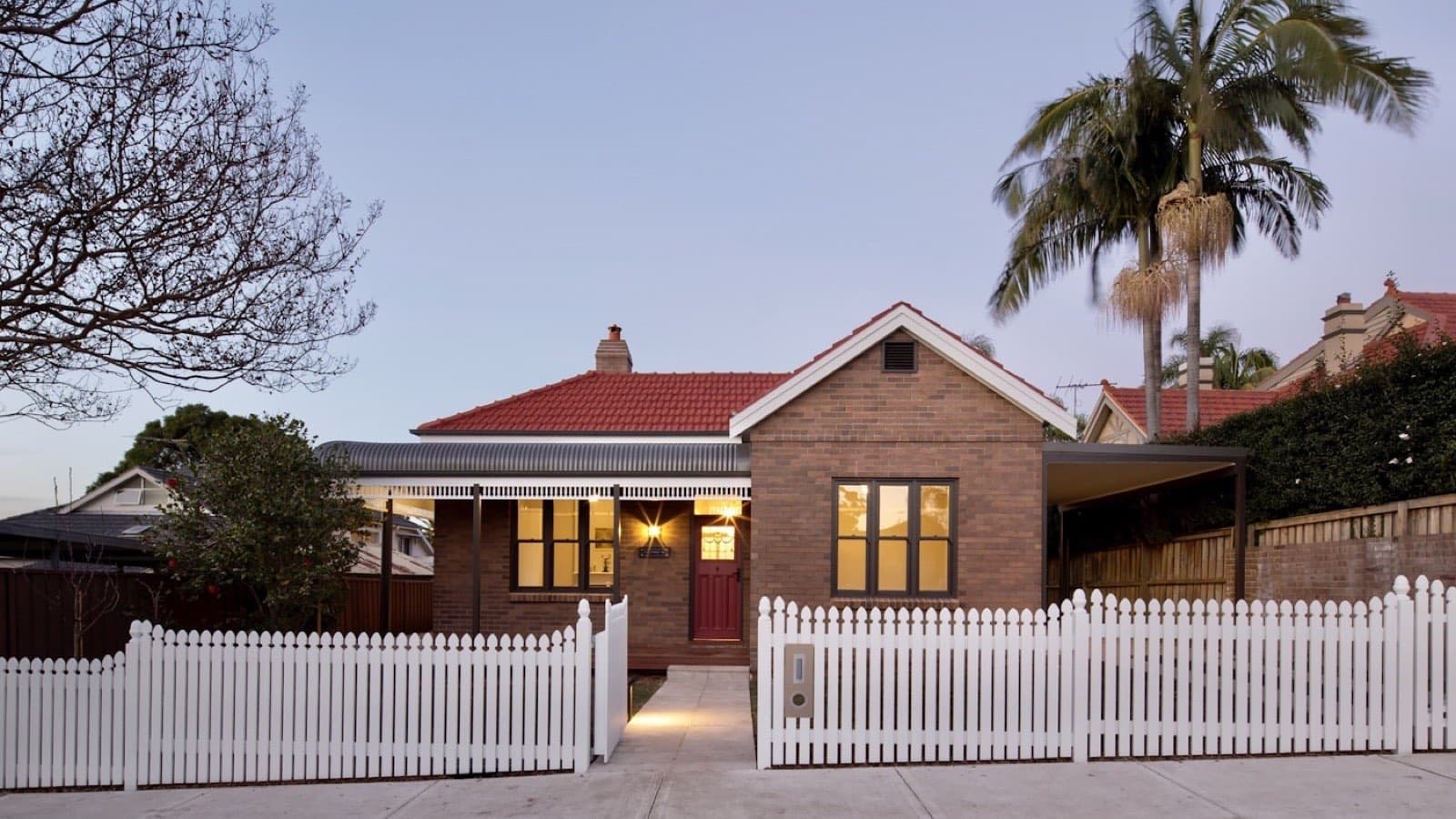 A single-storey house with a red roof behind a white picket fence