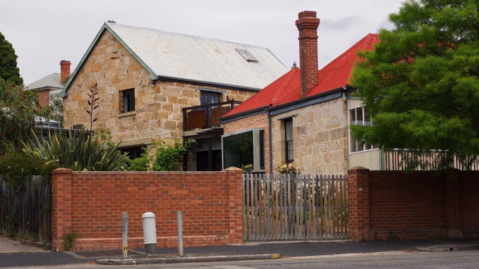 A large brick house with a red tiled roof behind a low fence