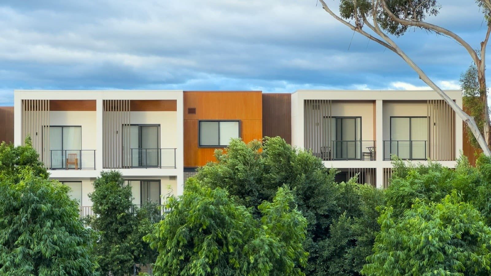 A modern apartment building with trees against a cloudy sky
